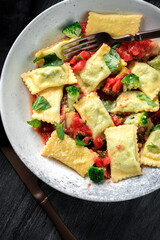Italian square ravioli with spinach, tomato sauce and broccoli in a plate on a black background. Dish pasta ravioli