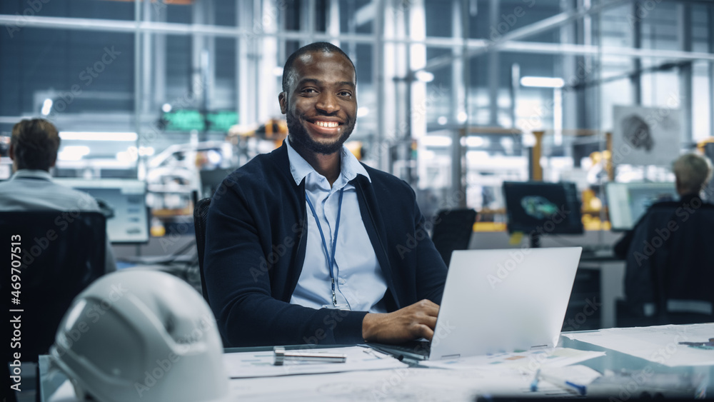 Poster portrait of a happy young african american engineer working on laptop computer in an office at car a