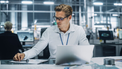 Young Handsome Engineer Working and Managing Projects on Laptop Computer in an Office at Car Assembly Plant. Industrial Specialist Working on Vehicle Parts in Technological Development Facility.