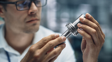 Close Up Portrait of Young Handsome Engineer in Glasses Working on Manufacturing Metal Parts in Office at Car Assembly Plant. Industrial Product Designer Examining Prototype Parts Before Production.