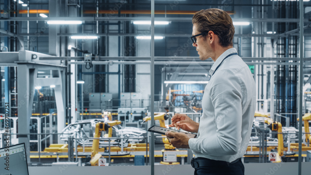 Poster handsome engineer in glasses and white shirt using tablet computer and looking out of the office at 