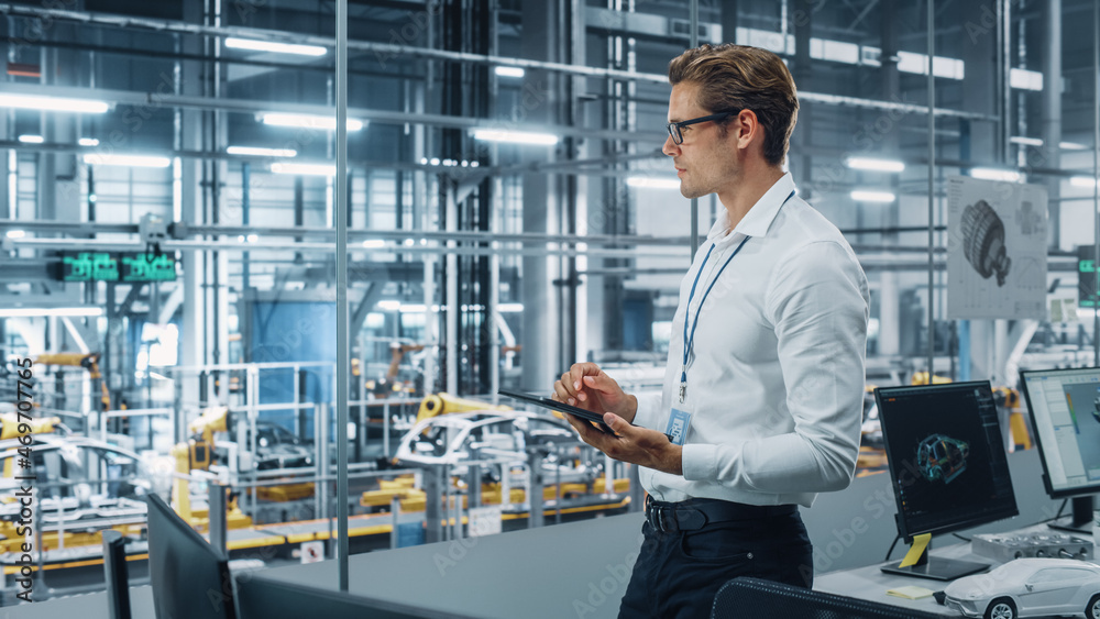 Poster handsome engineer in glasses and white shirt using tablet computer and looking out of the office at 
