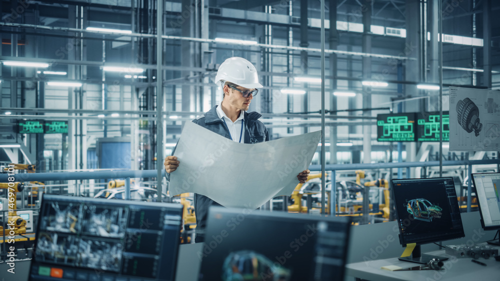 Fototapete engineer in uniform and hard hat looking at a technical blueprint at work in an office at car assemb
