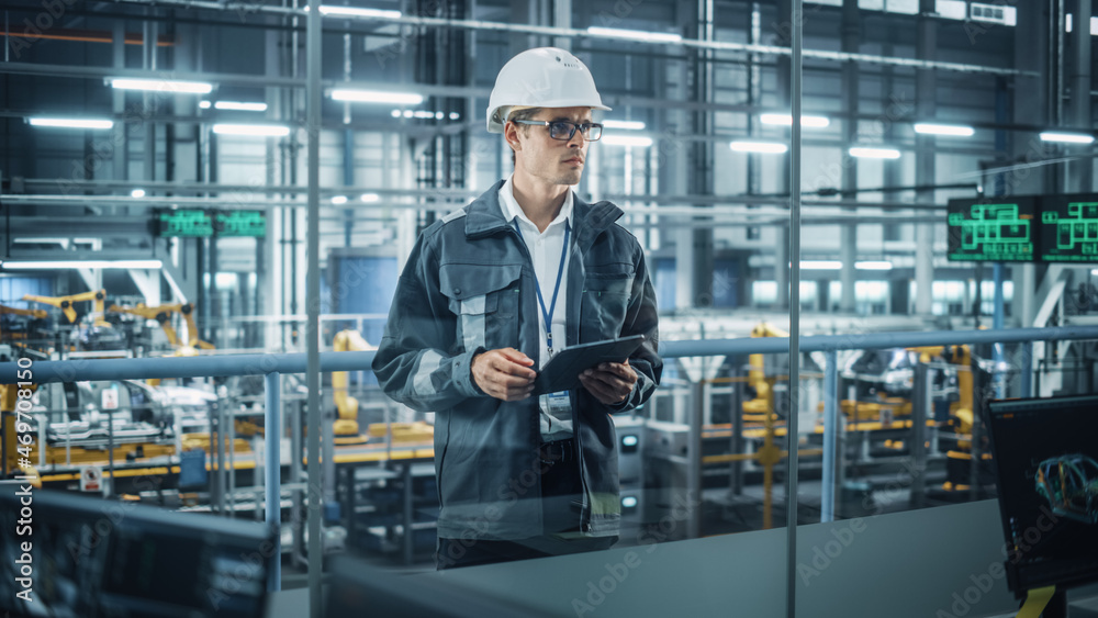 Aufkleber Handsome Engineer in Uniform and Hard Hat Using Tablet Computer at a Car Assembly Plant. Industrial Specialist Working on Vehicle Design, Overlooking Production in Technological Facility.