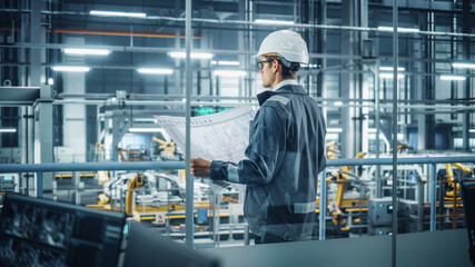 Engineer in Uniform and Hard Hat Looking at a Technical Blueprint at Work in an Office at Car Assembly Plant. Industrial Specialist Working on Vehicle Parts in Technological Development Facility.