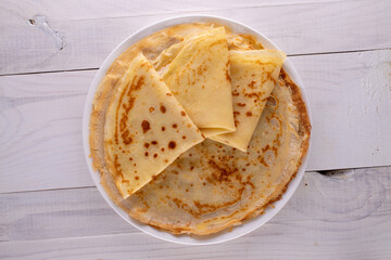 Several fragrant homemade pancakes on a ceramic plate on a wooden table, close-up, top view.