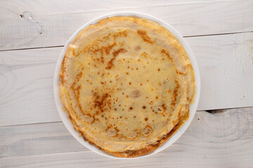 Several fragrant homemade pancakes on a ceramic plate on a wooden table, close-up, top view.