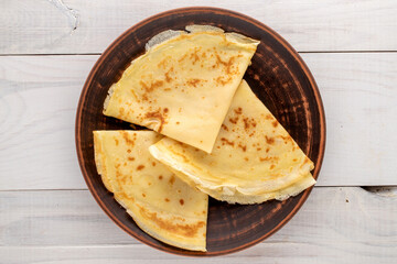 Several fragrant homemade pancakes on a ceramic plate on a wooden table, close-up, top view.