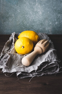 2 limones con un exprimidor manual de madera sobre una tela de lino gris, sobre una mesa de madera oscura
