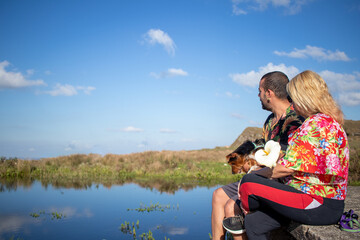 couple sitting by the lake, looking at the landscape, man holding a little black dog, sunny day with blue sky, close-up photo with space for text.