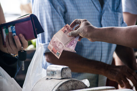 Mão de uma pessoa entregando dinheiro para efetuar um pagamento.