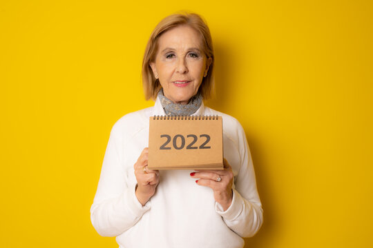 Mature Smiling Woman Showing Calendar Isolated Over Yellow Background.