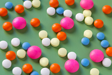 Tablets and vitamins of different shapes and colors on a green background. Medical education