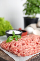 Raw chicken minced meat with basil on wooden board, closeup