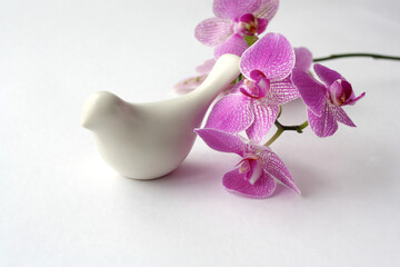 The figure of a white ceramic bird on a pink orchid background.