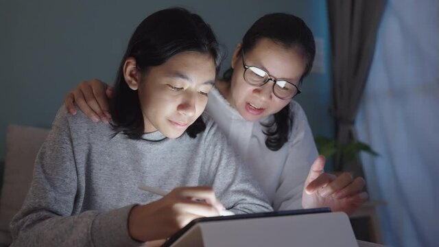 Happy family of Asian mother and daughter drawing with digital tablet at night