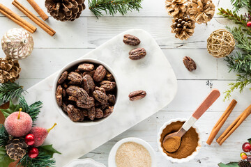 A bowl filled with candied pecans surrounded by Christmas decorations.