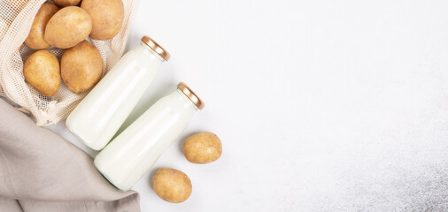 Vegan plant based milk in two bottles. Alternative potato milk and potato tubers on gray table. Top view. Copy space