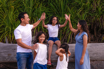 family, leisure and people concept-young active parents with three daughters with arms up- enjoying summer vacation together. Big asian happy family of five.