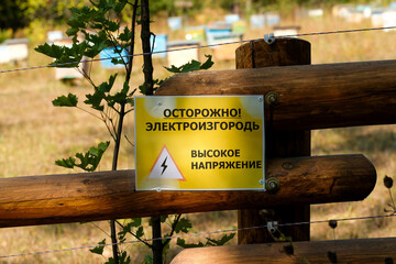 Warning on a wooden fence. Russian text: Caution. The fence is energized. High voltage