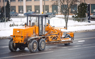 Snow removal machine, motor grader moving on city road, equipped with moldboard, plow and blades for snow and ice cleaning. Winter equipment for clear long stretches of road efficiently - obrazy, fototapety, plakaty