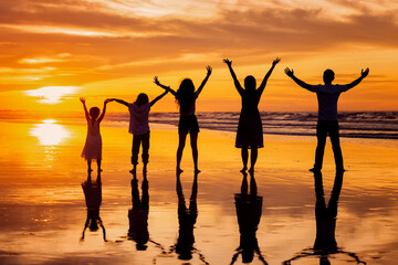 back view silhouette of happy family holding hands up and having fun together on tropical beach at summer sunset