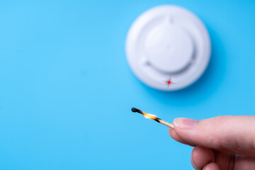 Burning match in a woman's hand and a fire detector on a blue background. Fire safety concept. Copy-space