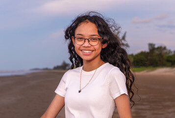 summer, childhood, leisure and people concept-portrait of pretty asian smiling teenager with long hair girl in eyeglasses on the beach
