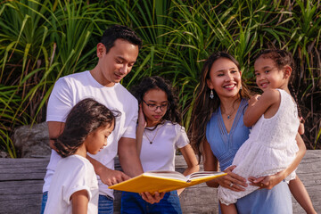 family, leisure and people concept-big asian happy family with three daughters reading the book, enjoying summer vacation together