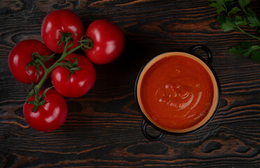 Tomato soup in a black bowl on brown background. Top view.
