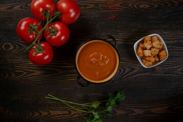 Tomato soup in a black bowl on brown background. Top view.