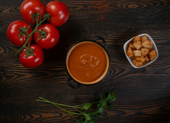 Tomato soup in a black bowl on brown background. Top view.