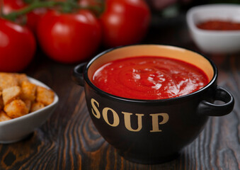 Tomato soup in a black bowl with the inscription Soup on a brown background.