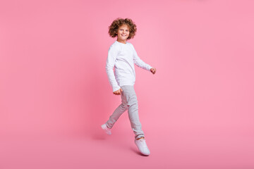 Fototapeta na wymiar Full size photo of positive happy small child jump up raise walk empty space isolated on pink color background
