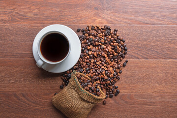 cup of coffee and coffee beans in a sack on Brown background, top view