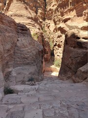 La cité nabatéenne Petra, située au sud de l'actuelle Jordanie, ancien chemin et marche sur des rochers rouges et oranges, forte chaleur et des cailloux, escalier rocheux dans l'ombre