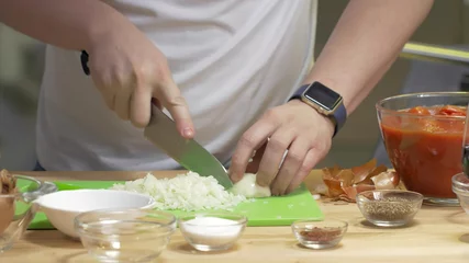 Foto op Canvas Young chef slices onion into pieces on aplastic chopping board. © nimito