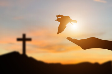 Close up image silhouette hand of woman praying and free bird enjoying nature on sunrise and crosses on hill  background.