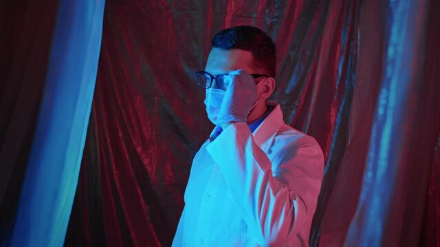 Portrait of a young handsome doctor wearing glasses and crossing hands in laboratory in emergency light