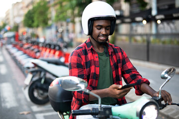 Handsome African man with scooter in the city. Young man using the phone.
