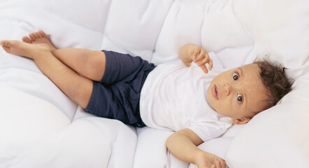 Little cheerful baby lies on a white soft mattress.  Happy childhood lifestyle.