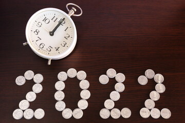 Fototapeta na wymiar The clock shows midnight. Number 2022 composed of coins on a dark wooden background. Metal silver coins. Happy New Year 2022.