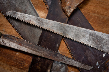 Old vintage metal saws for wood of different shapes and sizes, crumpled on a wooden background.