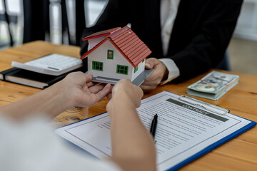 Fototapeta na wymiar Two people holding a small model house, the home salesman handing over the house to the customer after signing the contract and inspecting the house. Real estate trading ideas.