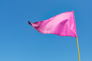 Pink sports flag on a flagpole fluttering in the wind against a clear blue sky