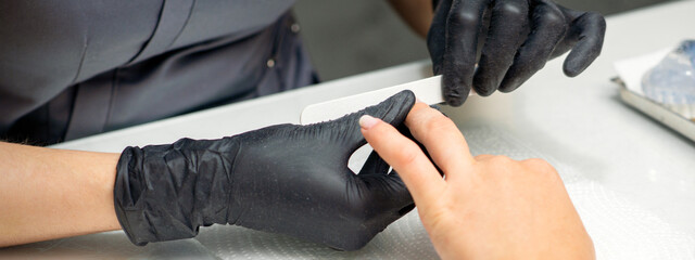 Woman receiving a manicure with nail file by a manicure master in a nail salon