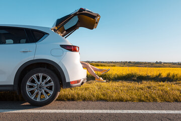woman legs stick out of suv car trunk parked at roadside of speedway