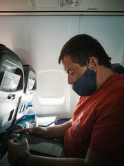A middle aged masked man on an airplane reading an e-book