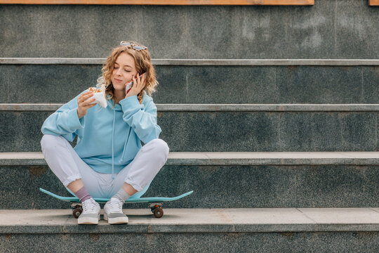 Young woman eating street food outdoors and talking on phone.