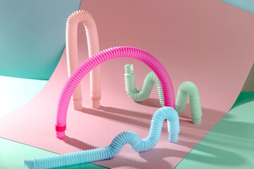 Pink antistress pop tube toy arch among curved shapes on pink and blue background with copy space.